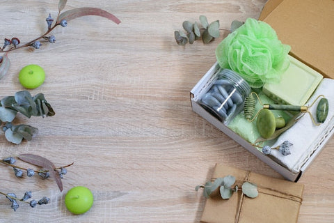 Geschenkbox mit grünem Badeschwamm, Seife, Jade-Roller, Kerzen, Eukalyptus auf Holz