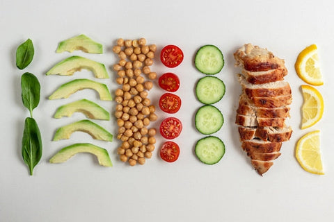Gesunde Zutaten wie Avocado, Kichererbsen, Tomaten, Gurke, Hähnchen und Zitrone ordentlich angeordnet