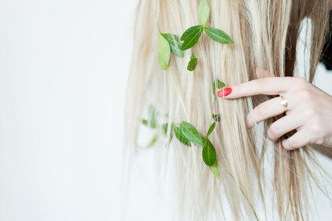 Blondes Haar mit grünen Blättern, Hand mit rotem Nagellack, natürliche Haarpflege