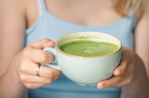 Frau hält Matcha Latte in Keramiktasse, Nahaufnahme Hände und grünes Getränk