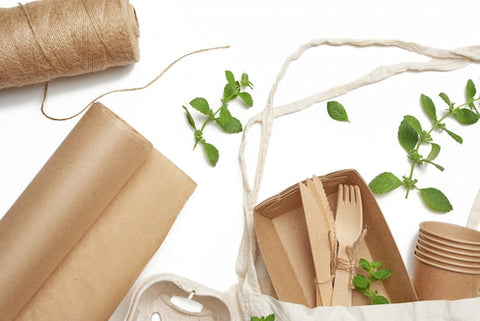 Nachhaltige Einwegverpackungen, Holzbesteck, Pappbecher, Papierrolle und grüne Blätter auf weißem Hintergrund