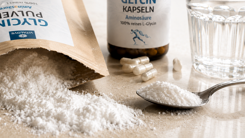 Glycin Pulver, Kapseln und Glas Wasser in heller Alltagsszene