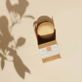 Festes Shampoo in Kartonverpackung auf beigem Untergrund, Naturkosmetik, Sonnenlicht