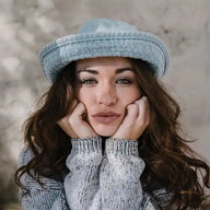 Frau mit langen braunen Haaren und hellblauem Hut trägt grauen Strickpullover, Nahaufnahme