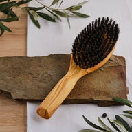 Haarbürste aus Olivenholz mit Naturborsten auf Stein, mediterran dekoriert