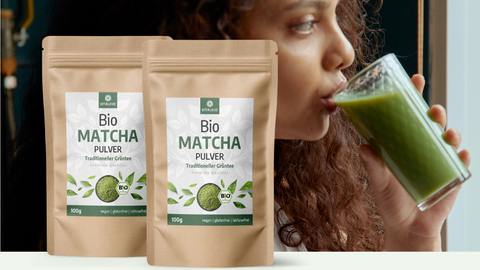 Zwei Packungen Bio Matcha Pulver und Frau, die einen frisch zubereiteten grünen Matcha-Smoothie trinkt