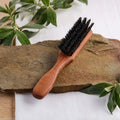 Bartbürste mit Holzgriff und schwarzen Borsten auf Stein, Naturdeko im Hintergrund