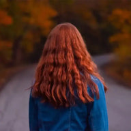 Frau mit roten Haaren in Jeansjacke geht auf herbstlicher Landstraße im Wald