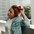 Junge Frau mit roten Haaren, Jeansjacke und weißem T-Shirt draußen auf Balkon