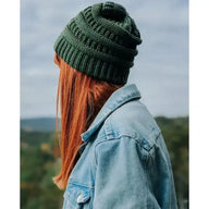 Frau mit grüner Strickmütze und Jeansjacke blickt in die Natur