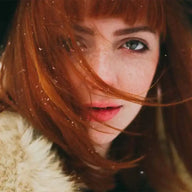 Rothaarige Frau mit Sommersprossen, Wintermantel und Schneeflocken im Haar, Porträtfoto